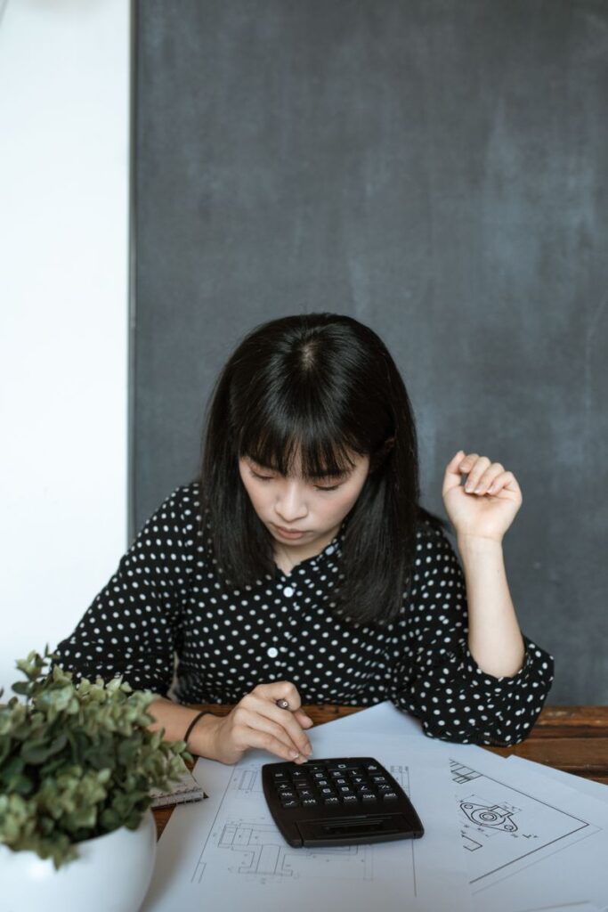 Asian woman calculating finance in modern office, focusing on documents and design work.