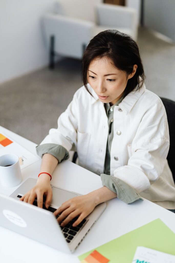 Young woman in office attire typing on laptop at a desk, focused on work.